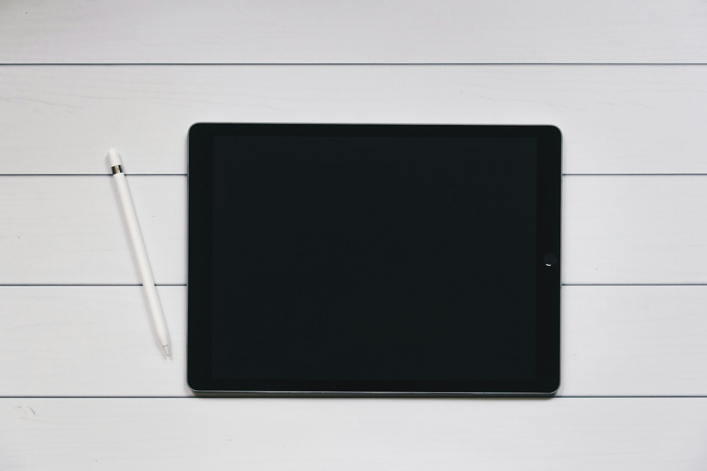 Black tablet and white stylus on a wooden plank.